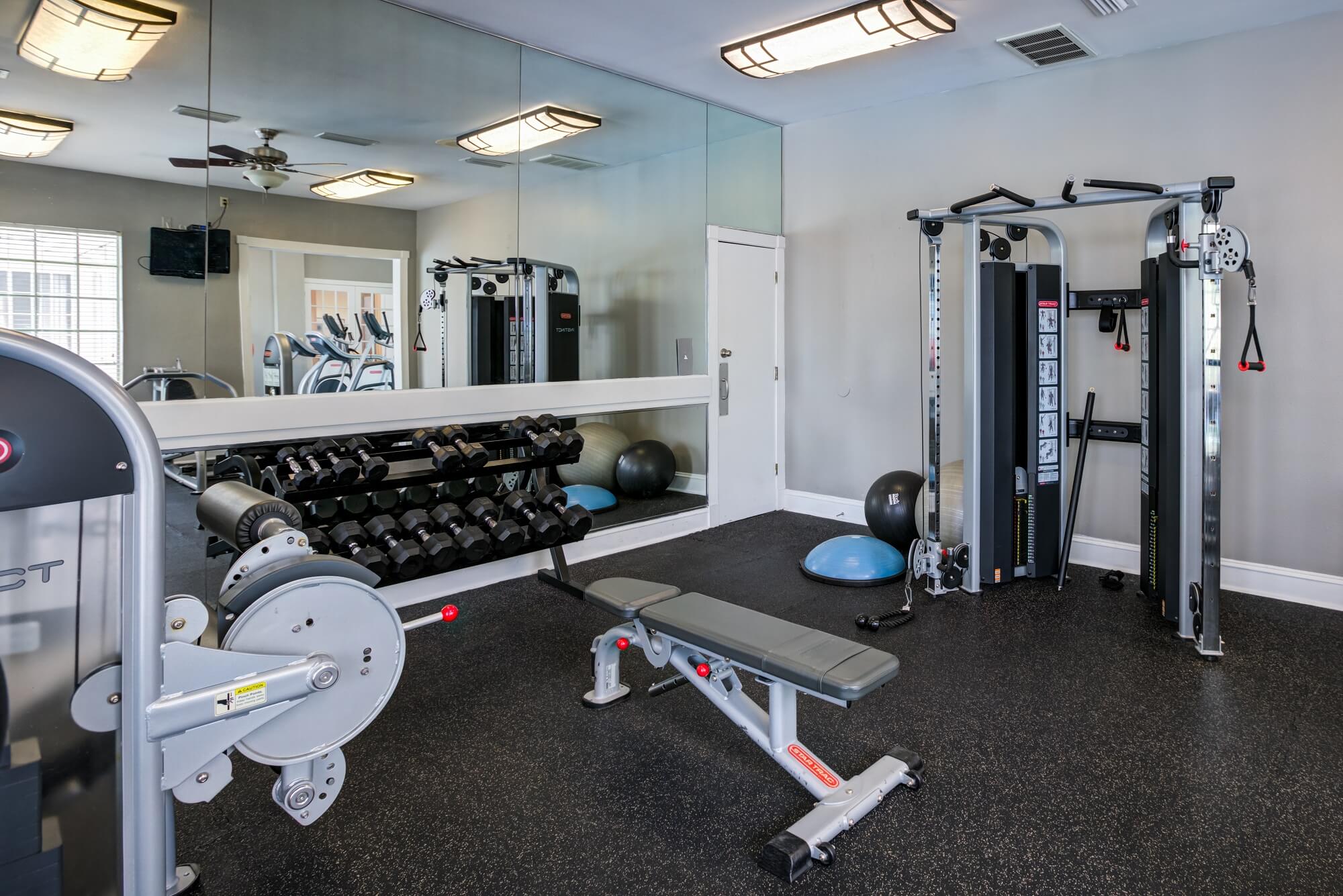 fitness center with mirrored wall, free weights, bench, and weight machines.